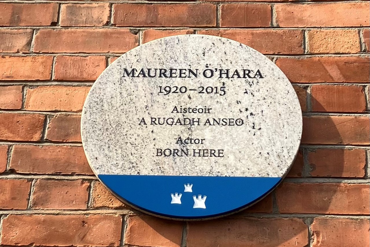 Photograph of a Dublin City Council commemorative plaque. The plaque is granite, with a blue base with the Dublin City logo, and is attached to a red brick wall. The text reads 'Maureen O'Hara 1920-1923, Aisteoir, A RUGADH ANSEO, Actor, BORN HERE.