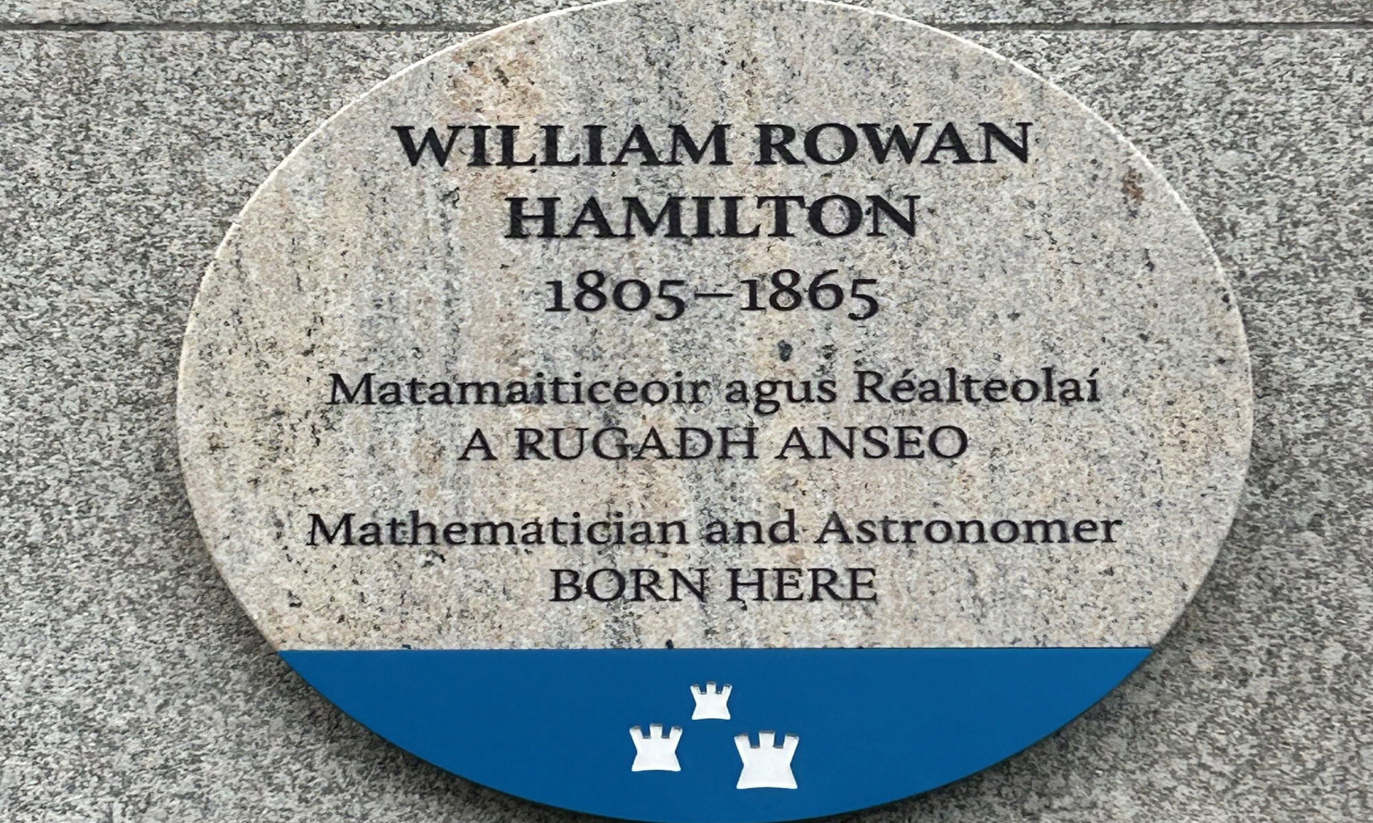 Photograph of a Dublin City Council commemorative plaque. The plaque is granite, with a blue base with the Dublin City logo, and is attached to a grey granite wall. The text reads 'WILLIAM ROWAN HAMILTON 1805-1865, Matamaiticeoir agus Réalteolaí, A RUGADH ANSEO, Mathematician and Astronomer, BORN HERE.