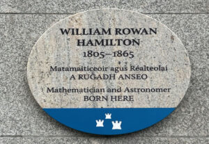 Photograph of a Dublin City Council commemorative plaque. The plaque is granite, with a blue base with the Dublin City logo, and is attached to a grey granite wall. The text reads 'WILLIAM ROWAN HAMILTON 1805-1865, Matamaiticeoir agus Réalteolaí, A RUGADH ANSEO, Mathematician and Astronomer, BORN HERE.